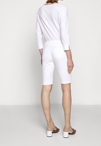 Bermudas de denim blanco con un ajuste slim, diseño de cinco bolsillos y puños enrollados, combinadas con sandalias de tacón marrones.