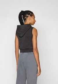 Felpa senza maniche nera con tasca frontale, realizzata con una texture morbida, dotata di cappuccio con coulisse e orlo aderente.