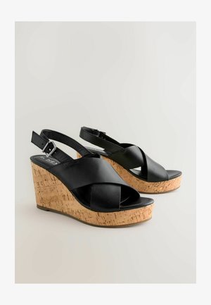 Black leather wedge sandals with crisscross straps and a cork platform. Buckle closure on the back strap; smooth texture.