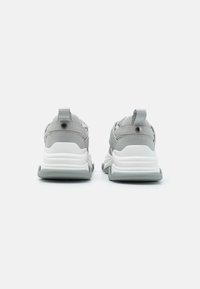 Baskets de sport grises avec une tige texturée, semelle en caoutchouc blanche, languettes au talon et détails de marque discrets.
