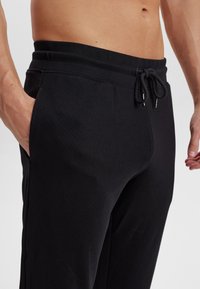 Sorte træningsbukser lavet af blødt stof med elastisk talje, snor lukning og sidelommer. Har en glat, strømlinet tekstur.