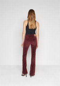 Pantalones acampanados de terciopelo burdeos con una textura sutil, cinturilla alta y bolsillos traseros, combinados con una camiseta sin mangas negra y sandalias de tacón negras.