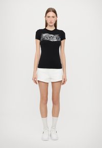 Must mustagaheline t-särk valge lainelise logo prindiga. Koos valgete lühikeste pükste ja valgete tossudega, lihtsa taustaga.
