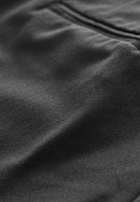 Gros plan sur un tissu noir avec une finition mate, une texture lisse et des lignes de couture à peine visibles. Comprend un détail de poche.