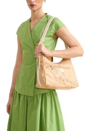 Donna con un vestito verde tiene una borsa a tracolla beige con stampa di una mappa del mondo vintage e tasca frontale con cerniera.