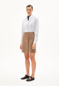 Gonna marrone a maglia con vita a coste e pieghe, abbinata a una camicia azzurra con bottoni e scarpe basse nere con un dettaglio circolare.