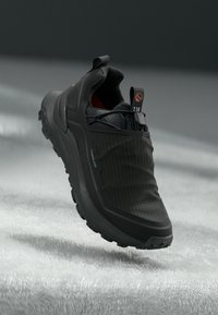 Sort sneaker med en glat gummisål, tekstureret stofoverdel med lodrette striber og en pull-tab ved hælen.