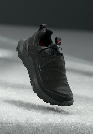 Black sneaker with a smooth rubber sole, textured fabric upper featuring vertical stripes, and a pull tab at the heel.