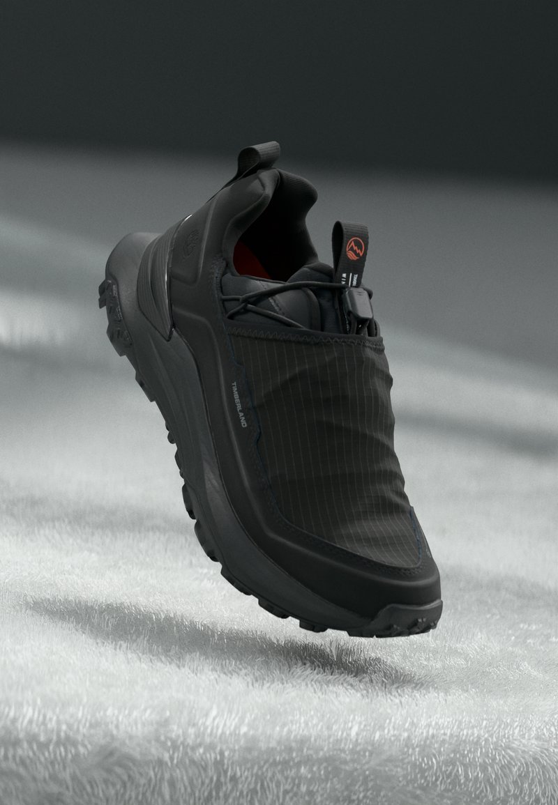 Sort sneaker med en glat gummisål, tekstureret stofoverdel med lodrette striber og en pull-tab ved hælen.