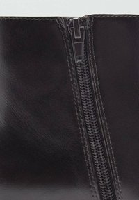 Bottines en cuir noir avec une fermeture éclair bien visible sur le côté, avec une texture lisse et des détails de couture contrastants.