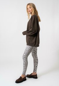 Sötétbarna, oversized pulóver hosszú ujjakkal, fehér leggingssel párosítva, amelyek fekete leopárdmintásak. Barna slip-on cipők.