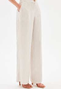 High-waisted, wide-leg trousers in a cream fabric with subtle vertical stripes. Features side pockets and a single button closure.