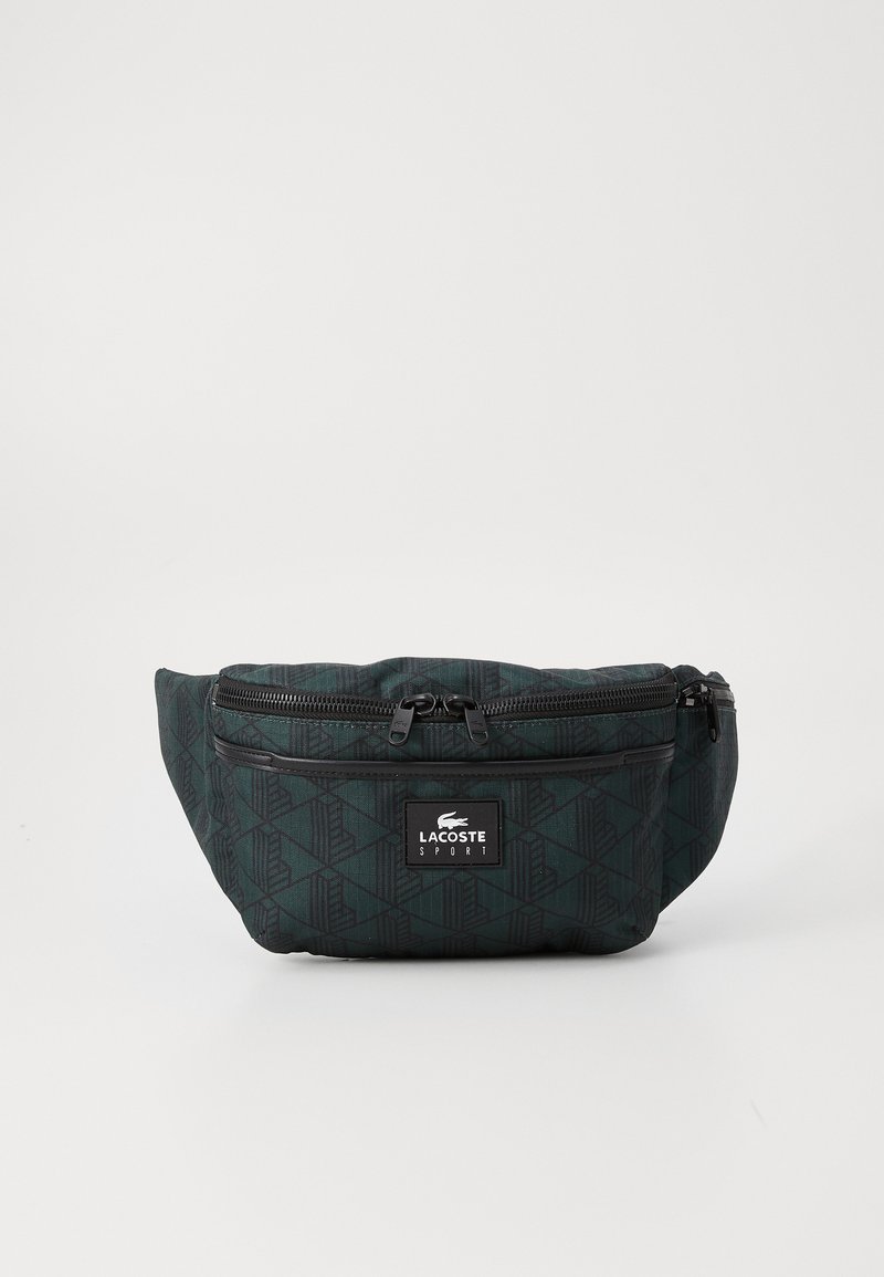 Juodas fanny pack'as su raštu, dviem užtrauktukais uždaromais skyriams, reguliuojama juosta ir Lacoste logotipu. Išsiskiria geometriniu dizaino tekstūru.