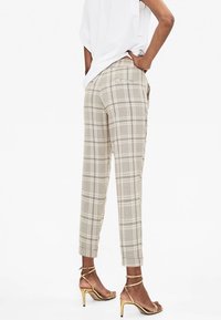 Pantalons à carreaux beiges avec une coupe fuselée, des chevilles retroussées et des poches latérales, accompagnés de talons hauts dorés à lanières.