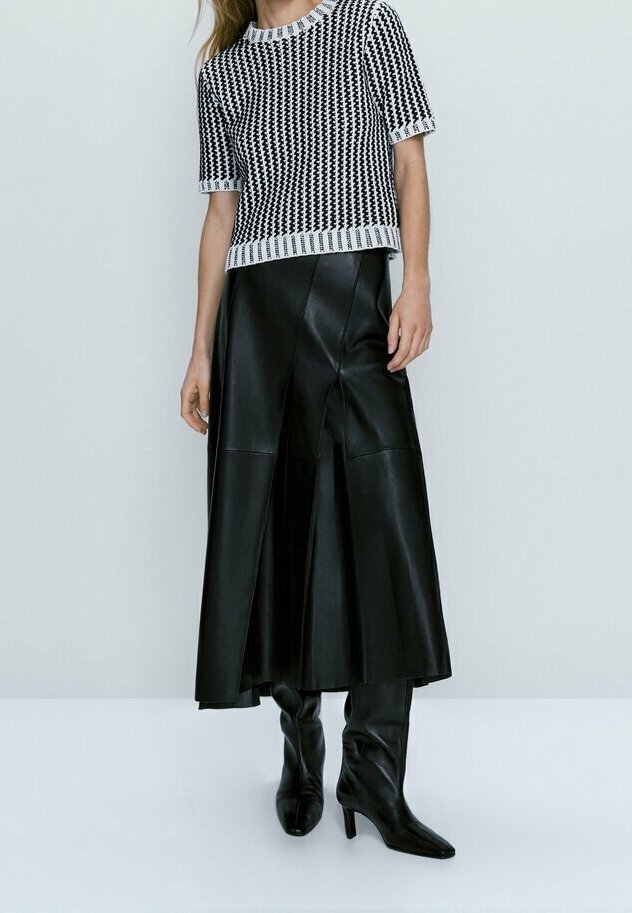 Femme portant un haut court à manches courtes à motifs noir et blanc, une longue jupe en cuir noire et des bottes à talons noires.