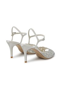 Sandali bianchi con tacco alto, cinturini sottili alla caviglia, un design floreale ritagliato e decorazioni in strass nella zona delle dita.