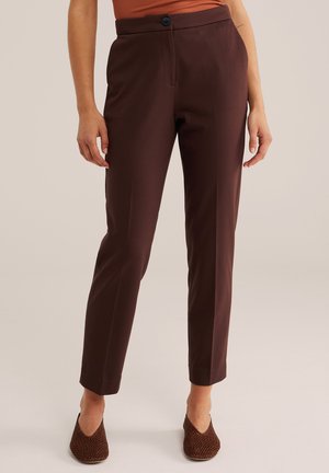 Pantalon brun ajusté slim longueur cheville porté avec des chaussures plates tissées marron et un haut couleur rouille.