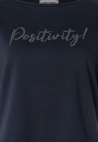 Navy-blaues T-Shirt mit kurzen Ärmeln aus weichem Material, das "Positivity!" in silbernen Strasssteinen über der Brust in einer Schreibschrift zeigt.