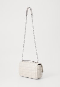 Borsa a tracolla crema trapuntata con forma rettangolare, tracolla in catena argentata e texture liscia. Caratterizzata da bordi arrotondati e zip nella parte superiore.