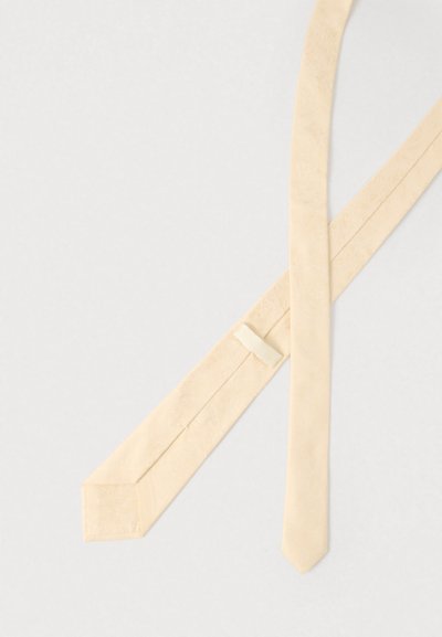 Béžová kravata s hladkou texturou a jemným květinovým vzorem. Má zúžený konec a poutko pro bezpečné upevnění.