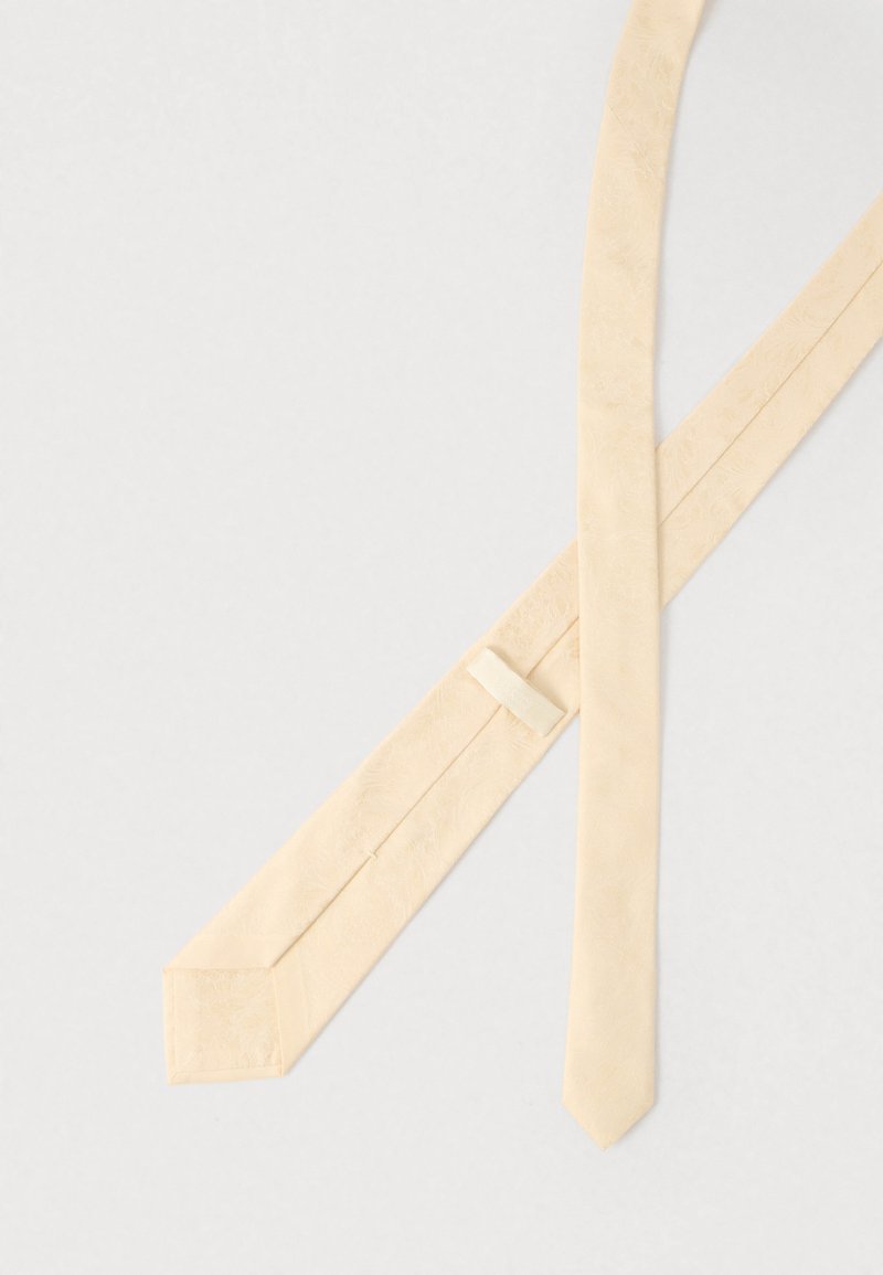 Beige slips med jämn textur och subtilt blommönster. Har en avsmalnande ände och en ögla för säker styling.