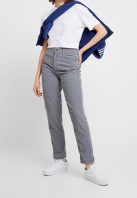 Grå kordflöjlsbyxor med rakt ben, tillsammans med en vit kortärmad t-shirt och en marinblå sweatshirt som hänger över axlarna. Vita sneakers.