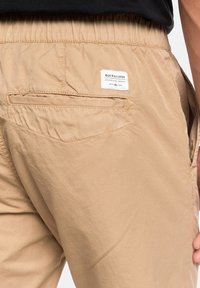 Ljusbeiga shorts i lätt tyg med elastisk midja, med en bakficka och en vävd etikett med varumärkesinformation.