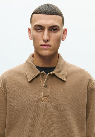 Barna pamut polo ing texturált felülettel, gallérral, gombos lezárással és egy kis logóval a bal oldalon felül.