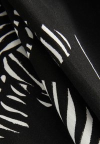 Tissu noir présentant un motif audacieux de feuilles blanches et de rayures, mettant en valeur une texture lisse et des plis superposés pour une dimensionnalité.