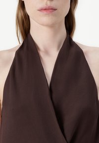 Pruun alusseeliku särk, millel on pehme ja koonuseline tekstuur, sügava V-kaelusega disain. Kangas näib kerge ja sile, ilma nähtavate kaunistusteta.