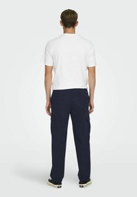 MarineblaueCargo-Hosen mit mehreren Seitentaschen, kombiniert mit einem schlichten weißen T-Shirt. Glatte Stofftextur, lockere Passform und klassischer Stil.