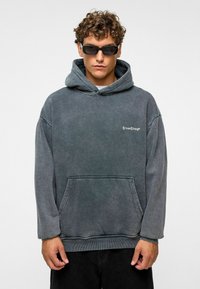 Grijze oversized hoodie met een trekkoordkap, een voorzak en een logo. Gemaakt van zacht materiaal, met ribgebreide manchetten en een zoom.