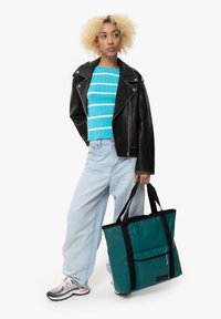 Borsa a tracolla teal con dettagli neri. Tessuto testurizzato, tasca con zip sul davanti, due manici resistenti. Abbinata a una giacca di pelle nera e una maglietta a righe blu.