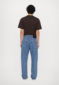 Braunes kurzärmliges Hemd und hellblaue, weit geschnittene Jeans mit einem schwarzen Etikett; die Jeans verfügen über zwei Gesäßtaschen und bestickten Text.