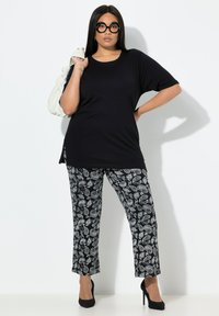 Černý top s krátkým rukávem spojený s černo-bílými kalhotami s paisley vzorem. Modelka drží bílou kabelku a má na sobě černé podpatky.