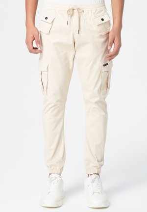 Pantalons cargo beiges avec une taille élastique, cordon de serrage, plusieurs poches latérales et bas resserrés. Fabriqués à partir de tissu léger.