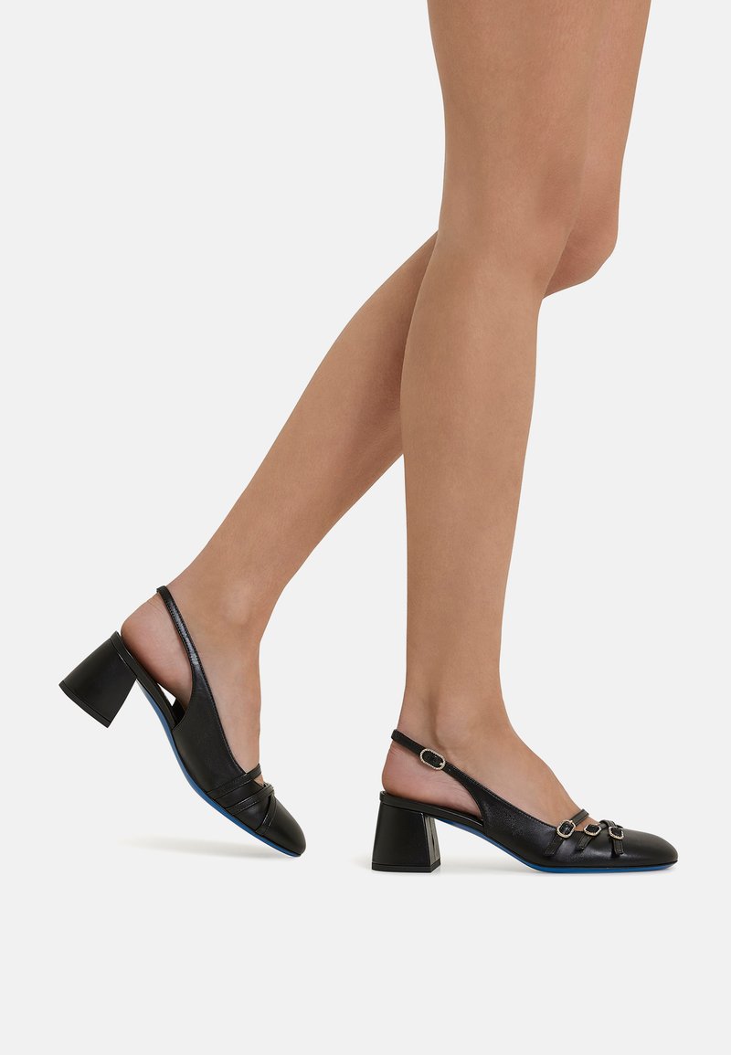 Tacchi slingback neri con punta quadrata, tacco spesso e dettagli metallici decorativi. Texture in pelle liscia e dettaglio della suola blu.