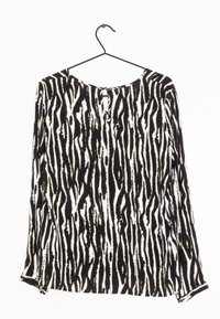 Maglietta a maniche lunghe appesa a un gruccia, caratterizzata da un motivo a strisce zebra bianco e nero con dettagli dorati, scollatura rotonda e apertura a chiave sul retro.