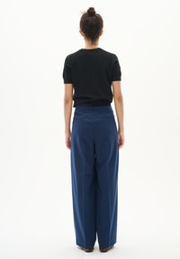 Schwarzes Short-Sleeve-Top, kombiniert mit hochgeschnittenen, weit geschnittenen blauen Hosen. Der Stoff wirkt glatt, mit einer taillierten Passform und minimalistischem Design.