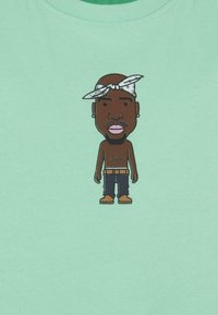 Mintgrünes T-Shirt mit einem Cartoon-Charakter, der ein Bandana trägt, blaues Jeans und beige Schuhe anhat, zentral auf dem Stoff gedruckt.