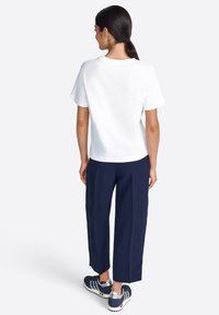 T-shirt blanc à manches courtes associé à un pantalon large bleu marine et des chaussures de sport grises. Tissu lisse, design simple et coupe décontractée.
