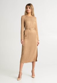 Długa, beżowa sukienka z długimi rękawami, okrągłym dekoltem, paskiem w talii i rozporkiem po boku. Gładki materiał o eleganckim fasonie.