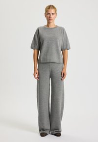 Maglione grigio a maglia con maniche corte e collo rotondo, abbinato a pantaloni grigi a gamba larga. Texture liscia e silhouette rilassata.