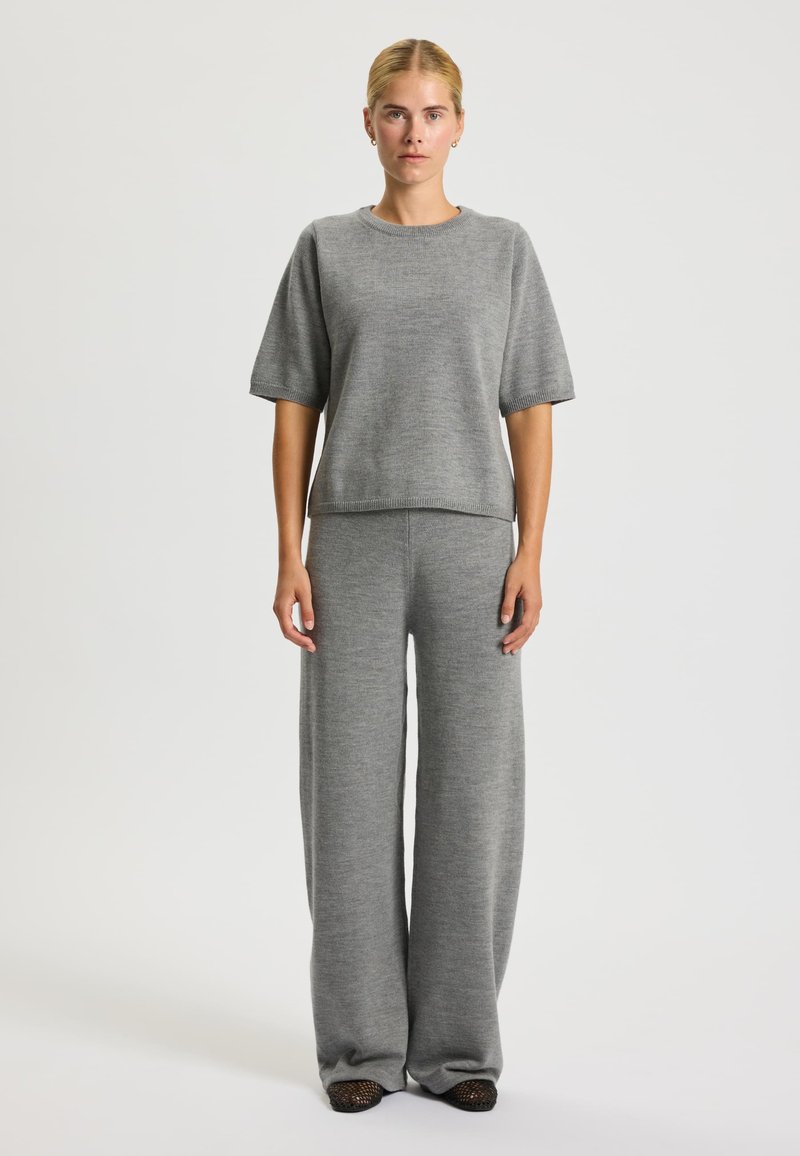 Maglione grigio a maglia con maniche corte e collo rotondo, abbinato a pantaloni grigi a gamba larga. Texture liscia e silhouette rilassata.