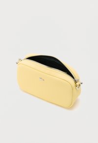 Gul kosmetiktaske med lynlås, tekstureret overflade, sølvfarvet beslag og mørkt indre. Rektangulær form med afrundede kanter.