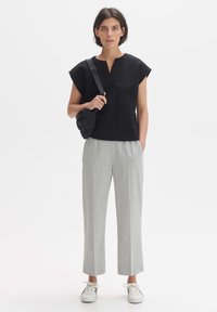 Zwart textuur top met korte mouwen en een V-hals, gecombineerd met lichtgrijze cropped broeken. Het model draagt een kleine zwarte gewatteerde tas en witte sneakers.