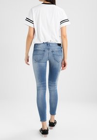 Smala jeans i ljusblå denim, med blekta fläckar och subtila slitna detaljer. Kombineras med en vit T-shirt med svarta ränder.