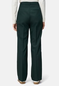 Pantalons larges verts en tissu lisse, avec des plis devant et derrière, et deux poches à l'arrière. Dispose d'une taille haute et d'une coupe ajustée.