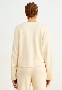 Beige fleece trui met een relaxte pasvorm, ronde halslijn en lange mouwen. Zachte textuur, cropped lengte en minimale naden op de achterkant.