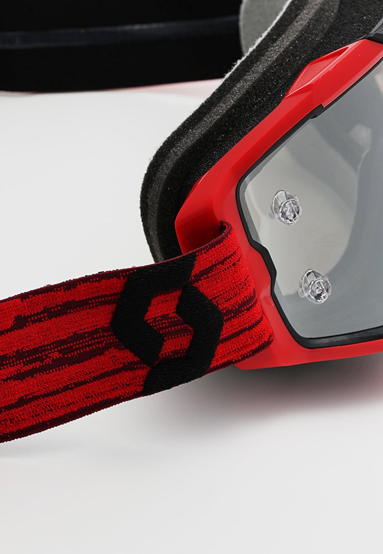 Skibrille mit rotem Rahmen und weicher Schaumstoffpolsterung, ausgestattet mit einem strukturierten schwarz-roten Band mit Logodruck und klaren Gläsern.